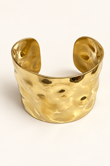 Wide hammered brass cuff on an ivory background.