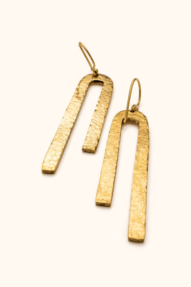 Upinde Hammered brass earrings on a light background.