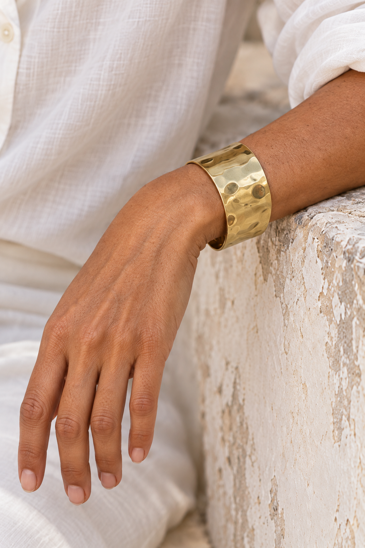 Close-up of the hammered brass cuff worn beside a weathered plaster railing.
