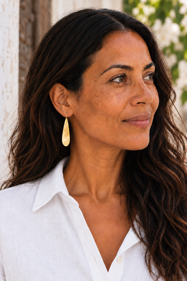 Close-up of a tapered hammered brass Machozi earring worn on the ear.