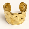 Wide hammered brass cuff on an ivory background.