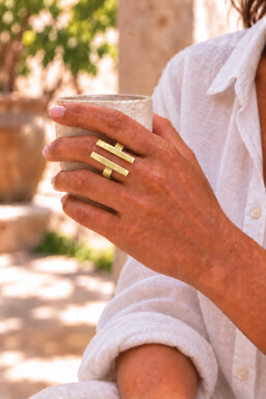 Jamaa Smooth brass ring worn while holding a ceramic cup, with a white linen shirt in a Lamu courtyard.
