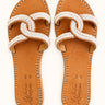 Overhead view of a pair of Criss Cross White beaded leather sandals on a cream background.